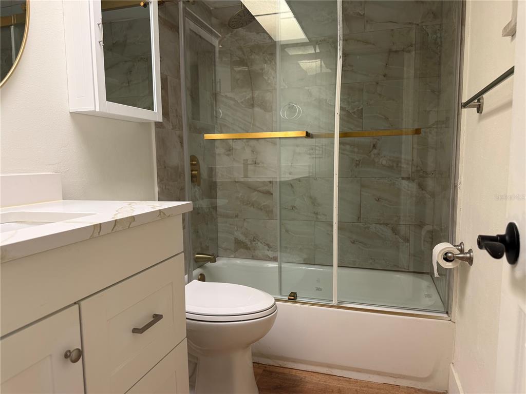 A bathroom features a white vanity, a toilet, and a shower-tub combo with tiled walls — 1001 77TH AVENUE N UNIT 102, ST PETERSBURG, FL