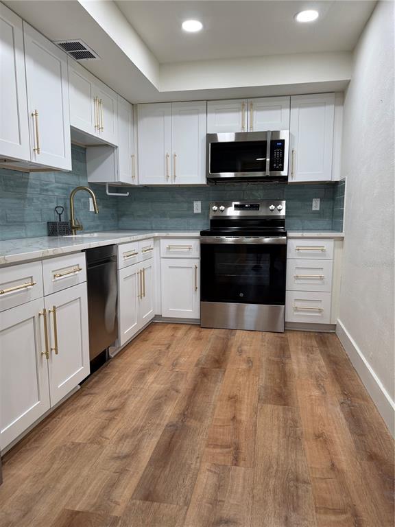 A kitchen features white cabinets, gold hardware, stainless steel appliances, and a blue tile backsplash — 1001 77TH AVENUE N UNIT 102, ST PETERSBURG, FL