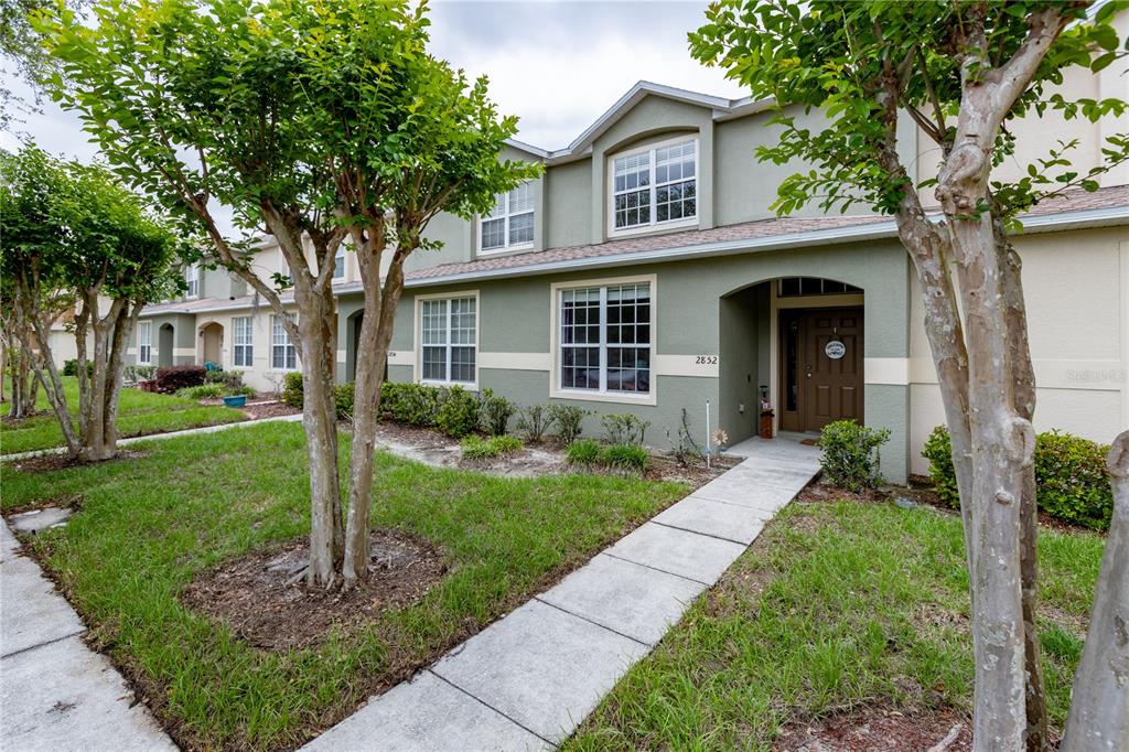 A two-story townhouse with a green exterior, a front walkway, and mature trees — 2852 TANZANITE TERRACE, KISSIMMEE, FL