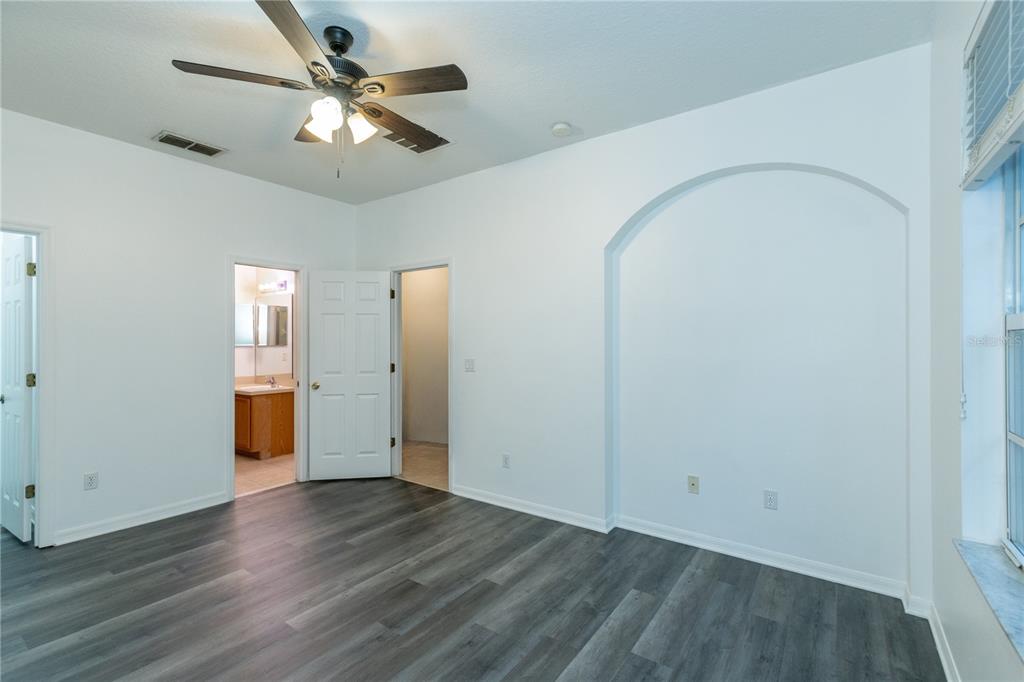 A bedroom with gray wood-look flooring, a ceiling fan, and an arched wall niche — 2852 TANZANITE TERRACE, KISSIMMEE, FL