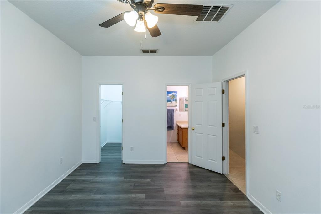 A bedroom with gray wood-look flooring, a ceiling fan, and three doorways leading to other rooms — 2852 TANZANITE TERRACE, KISSIMMEE, FL