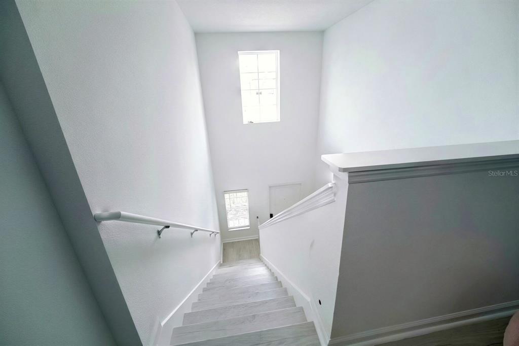 A staircase with light wood-look steps and a white handrail leads to a lower landing — 2185 AQUIFER LANE, DAVENPORT, FL