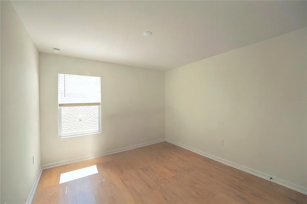 An empty bedroom with light-colored walls, wood-look flooring, and a single window — 2185 AQUIFER LANE, DAVENPORT, FL