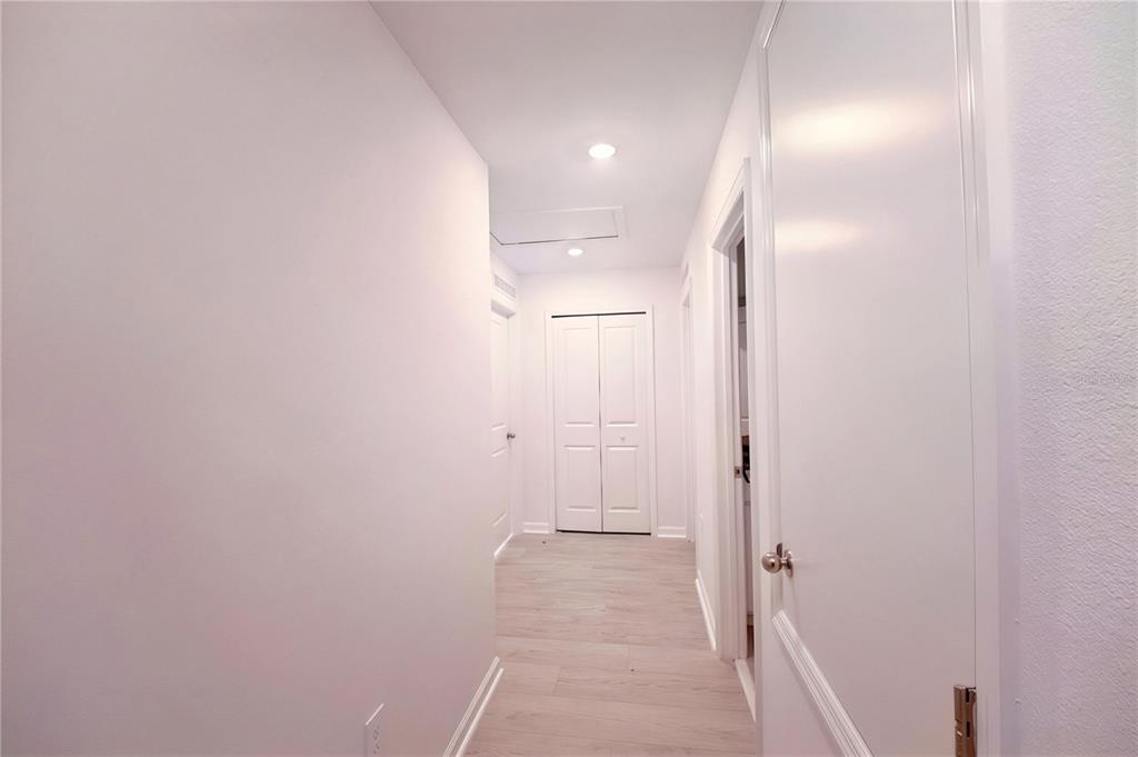 A hallway with light wood-look flooring, white walls, and several white interior doors — 2185 AQUIFER LANE, DAVENPORT, FL