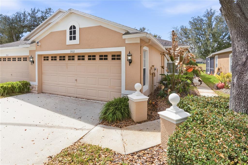 The exterior of a tan, single-story residential building with a two-car garage and landscaping — 19112 WHITE WING PLACE, TAMPA, FL