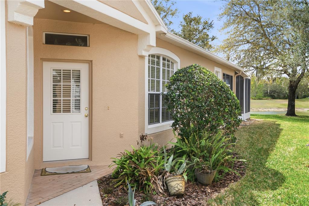 A beige house exterior features a white door, a window, and landscaping near a pond — 19112 WHITE WING PLACE, TAMPA, FL
