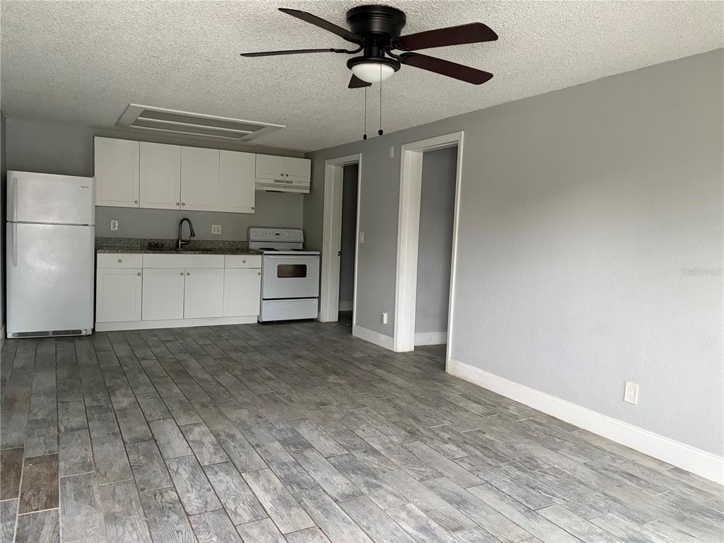 A kitchen with white cabinets and appliances opens into a living area with gray flooring — 1400 STRAWBERRY PLACE UNIT 12, PLANT CITY, FL