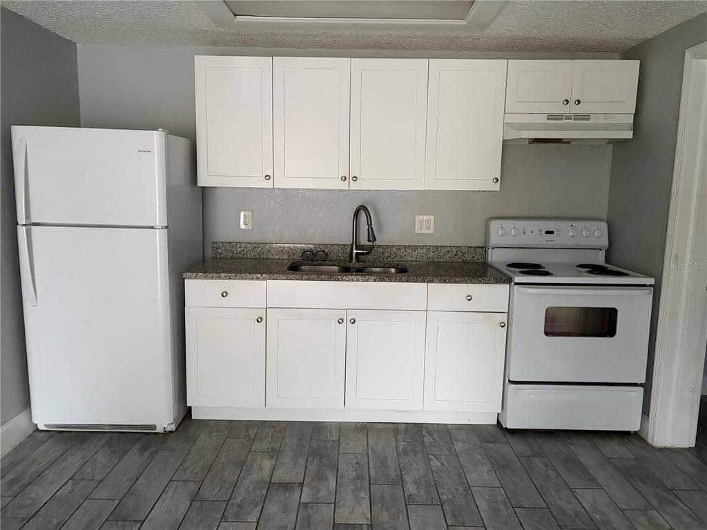 A kitchen features white cabinets, a white refrigerator, a white stove, and gray tile flooring — 1400 STRAWBERRY PLACE UNIT 12, PLANT CITY, FL