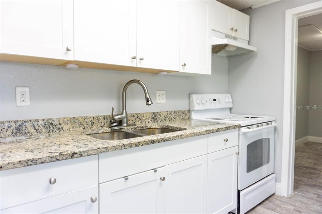 A kitchen features white cabinets, granite countertops, a stainless steel faucet, and a white stove — 1400 STRAWBERRY PLACE UNIT 12, PLANT CITY, FL