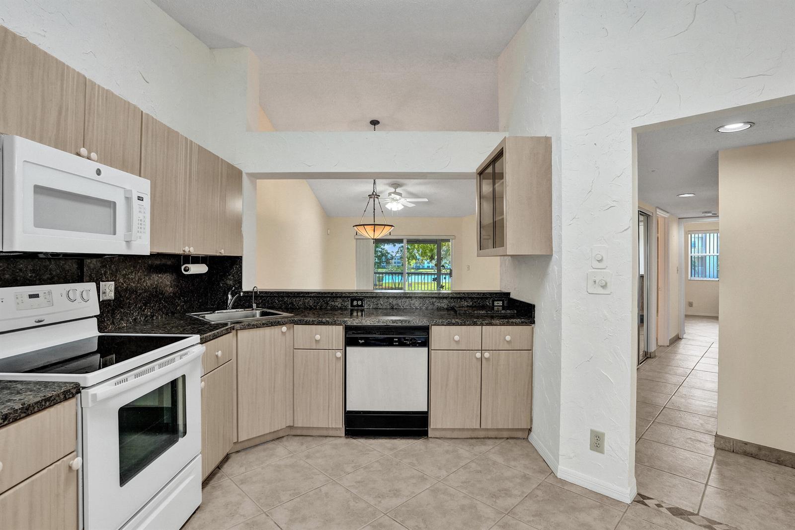 A kitchen with light wood cabinets, dark countertops, and a view into the living area — 7243 S Devon Drive, Tamarac FL 33321, TAMARAC, FL