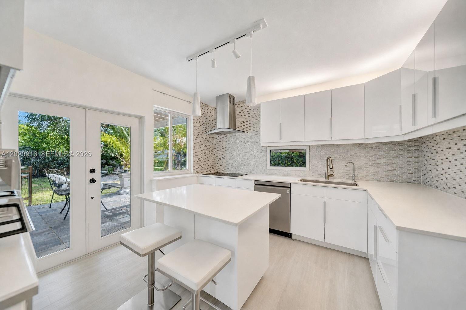 A modern white kitchen features a central island, stainless steel appliances, and a glass door — 860 NE 127TH ST, North Miami FL 33161, NORTH MIAMI, FL