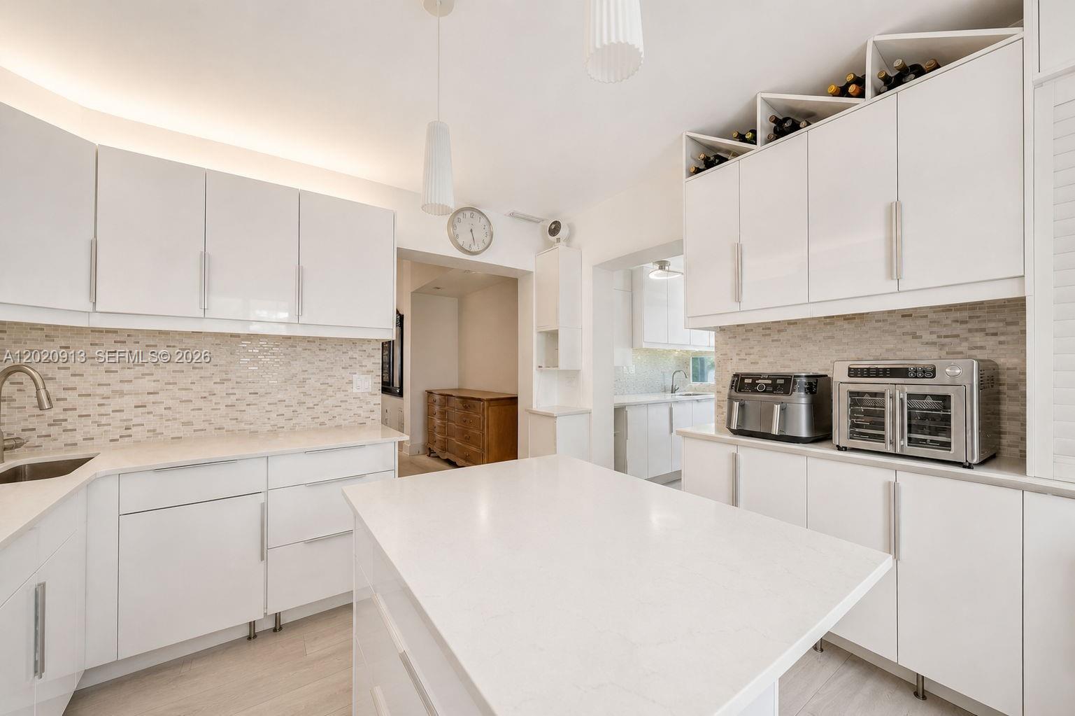 A modern white kitchen features an island, quartz countertops, and a tiled backsplash — 860 NE 127TH ST, North Miami FL 33161, NORTH MIAMI, FL