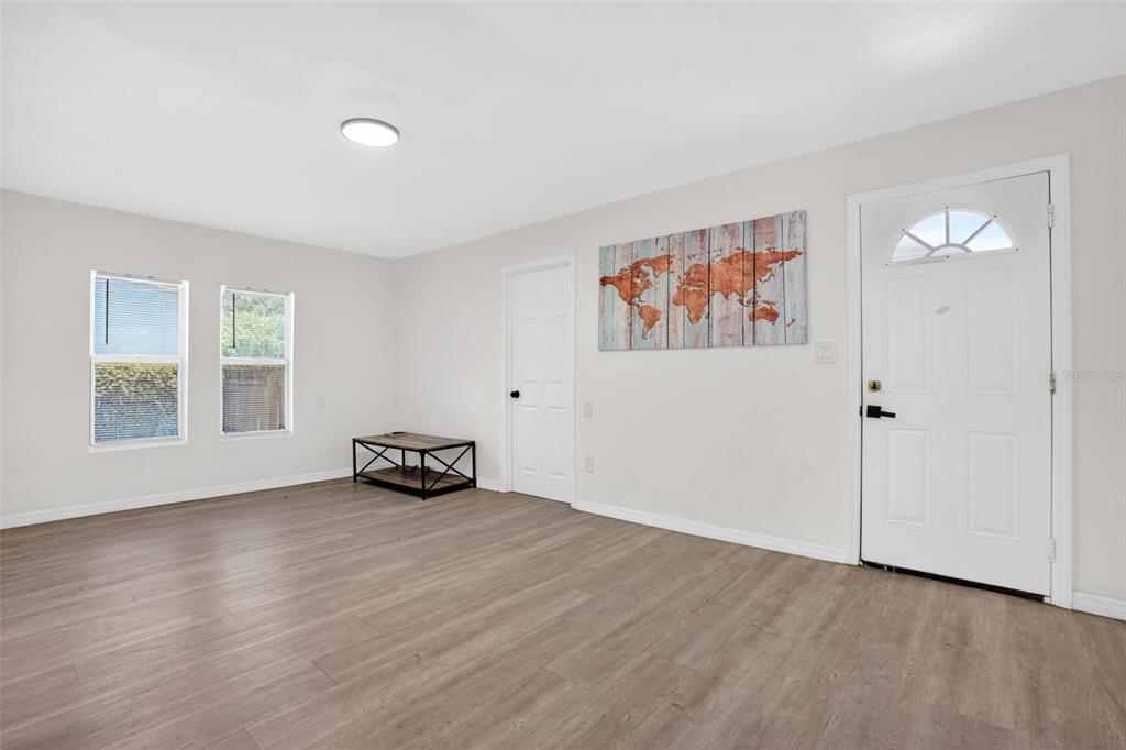 An empty living room features light gray walls, wood-look flooring, two windows, and a front door — 1717 18TH STREET S, ST PETERSBURG, FL