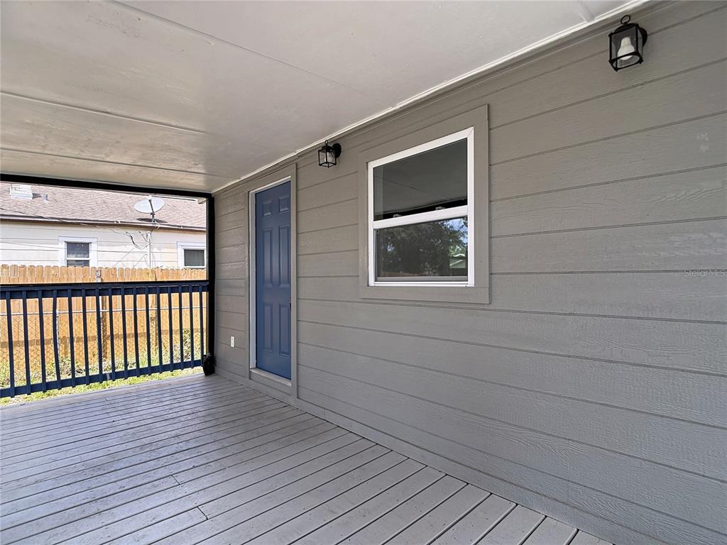 A gray-painted wooden deck features a blue door, a window, and two wall-mounted light fixtures — 9219 N 13TH STREET, TAMPA, FL