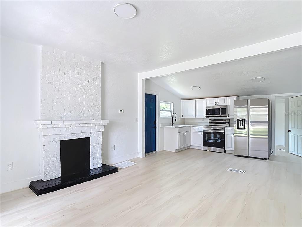 A living room with a white brick fireplace opens into a kitchen with stainless appliances — 9219 N 13TH STREET, TAMPA, FL