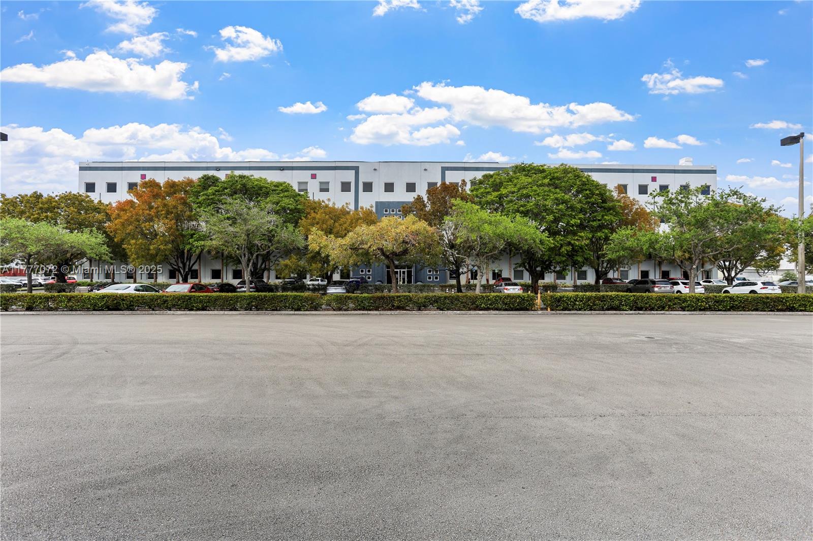 A large commercial building stands behind a parking lot and a row of trees — 7791 NW 46th St # 215, Doral FL 33166, DORAL, FL