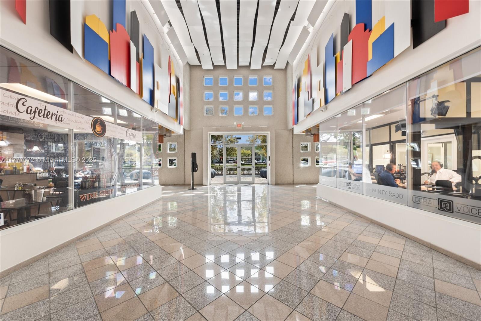 A bright, tiled lobby features glass-walled storefronts, colorful wall art, and a central entrance door — 7791 NW 46th St # 215, Doral FL 33166, DORAL, FL