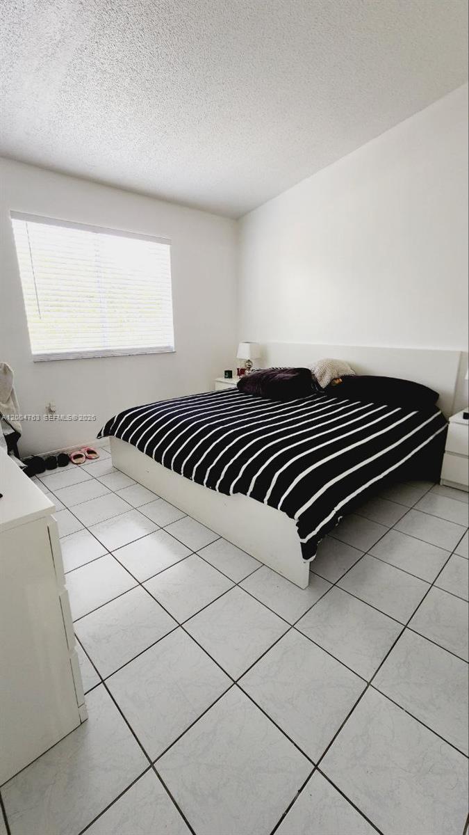 A bedroom with white walls, white tile flooring, and a bed with a striped comforter — 6960 NW 174th Ter # 706, Hialeah FL 33015, HIALEAH, FL