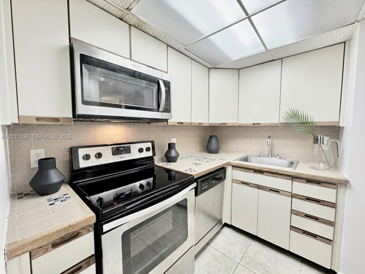 A kitchen features white cabinets, stainless steel appliances, tiled countertops, and a drop ceiling — 800 West Ave # 924, Miami Beach FL 33139, MIAMI BEACH, FL