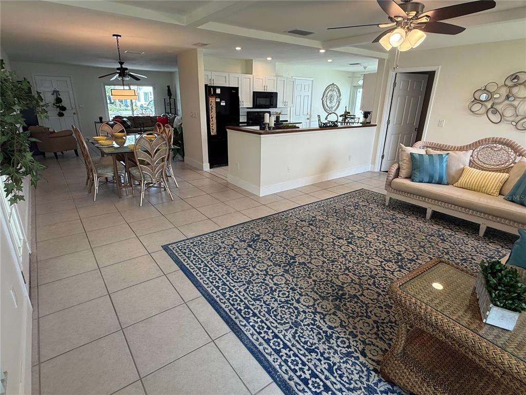 An open-concept living and dining area features tile flooring, a kitchen island, and wicker furniture — 9021 41ST WAY N UNIT 0, PINELLAS PARK, FL