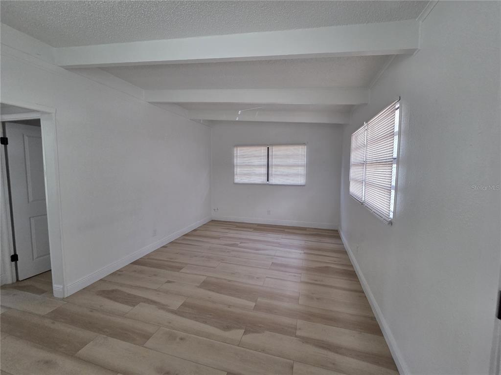 An empty living room features white walls, exposed ceiling beams, and light wood-look flooring — 3222 WELBORN WAY, TAMPA, FL