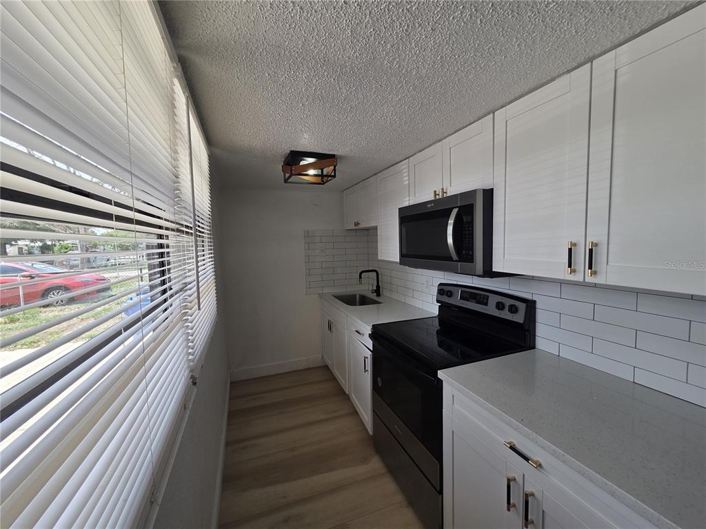 A narrow galley kitchen features white cabinets, stainless steel appliances, and light wood-look flooring — 3222 WELBORN WAY, TAMPA, FL