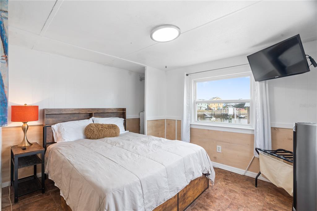 A bedroom features a bed, a bedside lamp, a wall-mounted television, and a waterfront view — 6501 CLARK STREET, HUDSON, FL