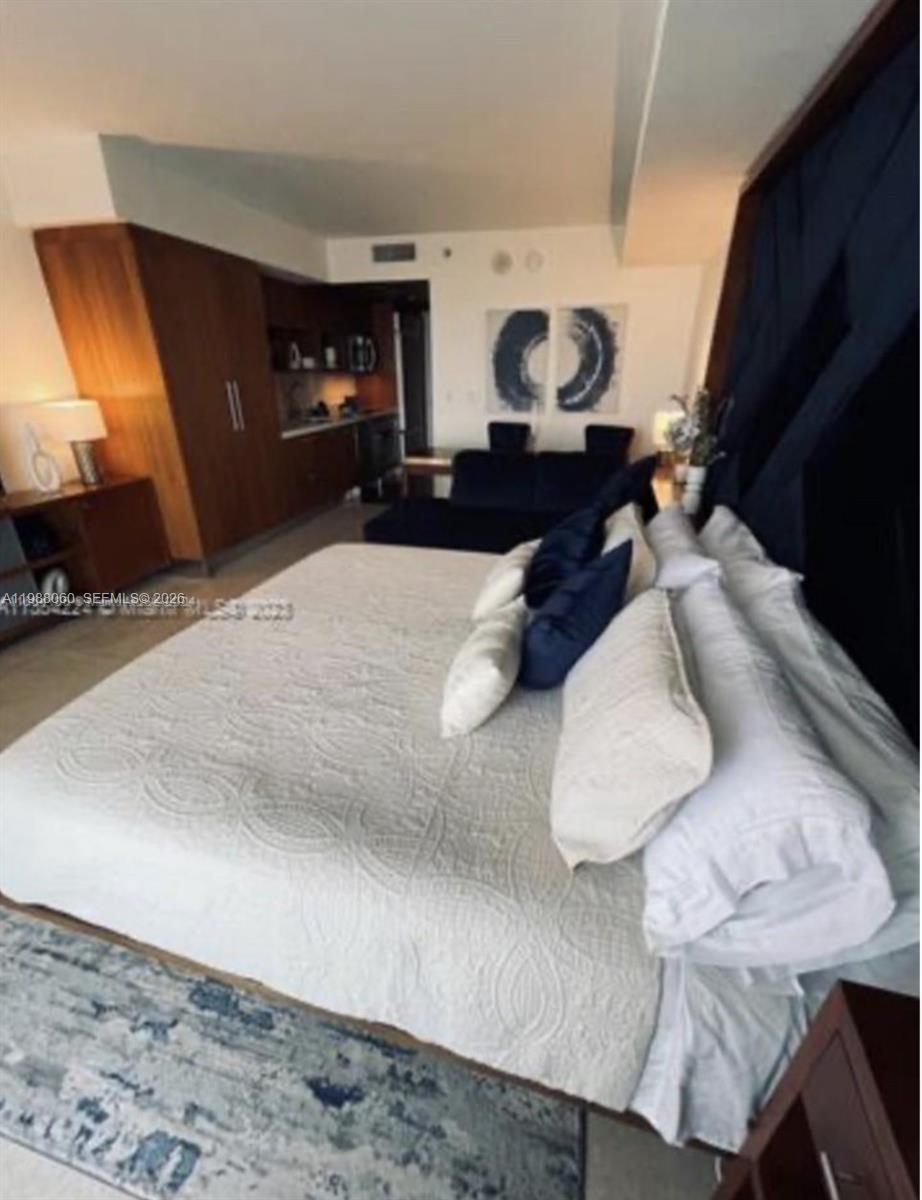 A bedroom with a large bed, dark wood cabinetry, and a small kitchenette area — 50 Biscayne Blvd # 607, Miami FL 33132, MIAMI, FL