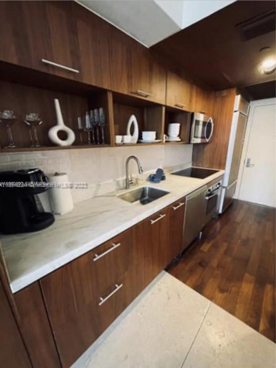 A galley kitchen features wood-toned cabinets, white marble-look countertops, and stainless steel appliances — 50 Biscayne Blvd # 607, Miami FL 33132, MIAMI, FL