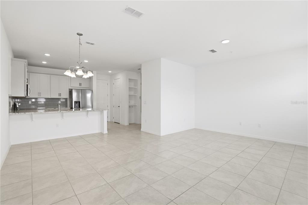 An open-concept kitchen with white cabinets and a breakfast bar overlooks a tiled living area — 11558 BUOY POINT PLACE, ORLANDO, FL