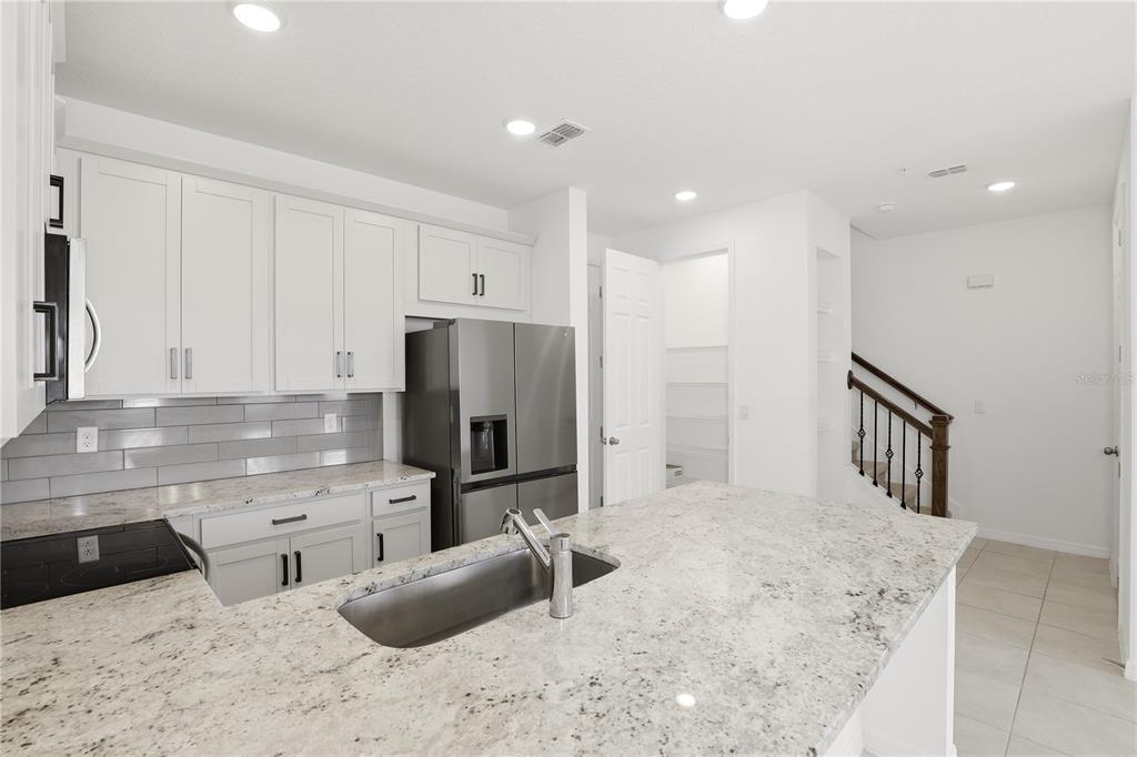 A kitchen features white cabinetry, granite countertops, a stainless steel refrigerator, and a center island — 11558 BUOY POINT PLACE, ORLANDO, FL