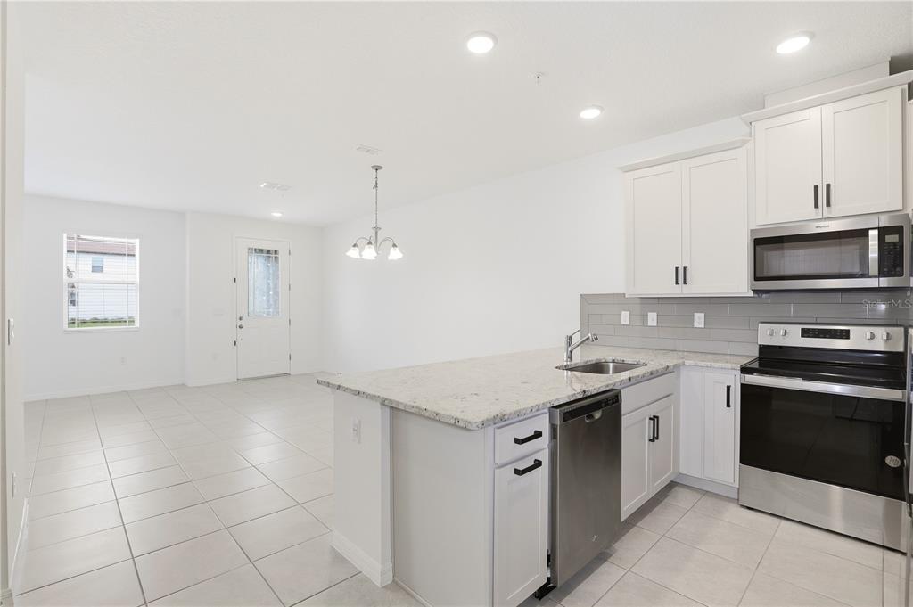 A kitchen with white cabinets, granite countertops, and stainless steel appliances opens to a dining area — 11558 BUOY POINT PLACE, ORLANDO, FL