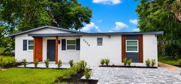 A single-story white house with a gray front door, wood accents, and a paved driveway — 5524 GAYMAR DRIVE, ORLANDO, FL