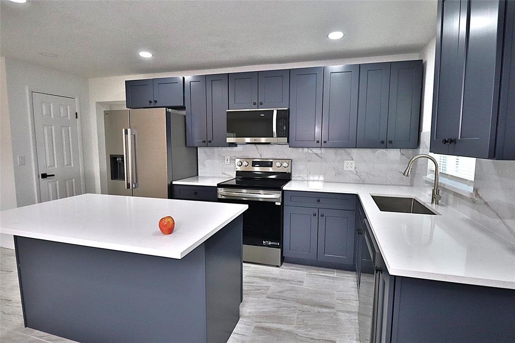 A kitchen features dark blue cabinets, white countertops, stainless steel appliances, and a center island — 5524 GAYMAR DRIVE, ORLANDO, FL