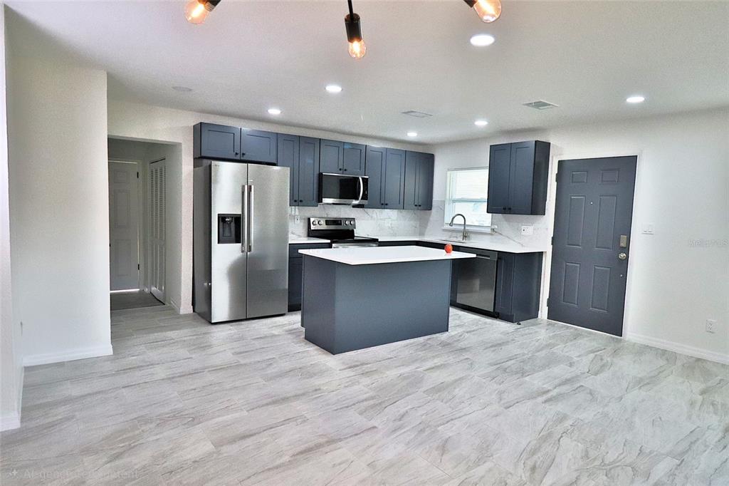 A kitchen features dark blue cabinets, stainless steel appliances, a center island, and light flooring — 5524 GAYMAR DRIVE, ORLANDO, FL