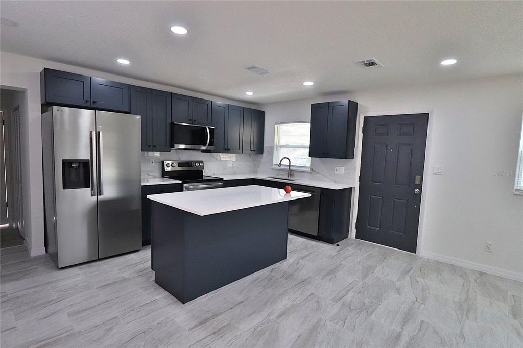 A kitchen features dark blue cabinets, stainless steel appliances, a white island, and light flooring — 5524 GAYMAR DRIVE, ORLANDO, FL
