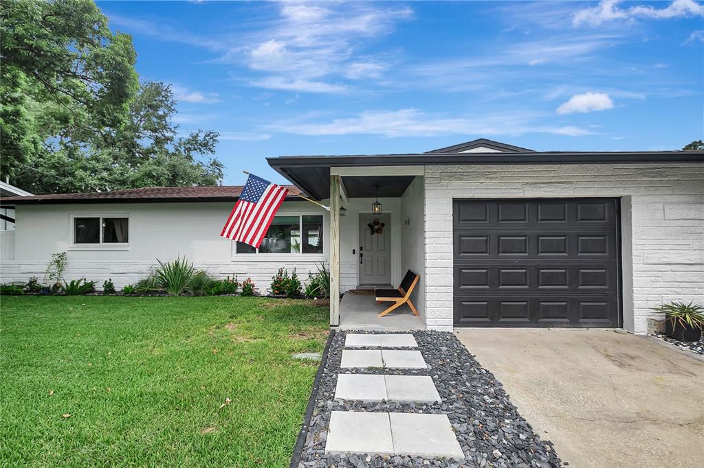 A white brick house with a dark garage door, a front porch, and a flag — 510 HILLCREST DRIVE, LARGO, FL