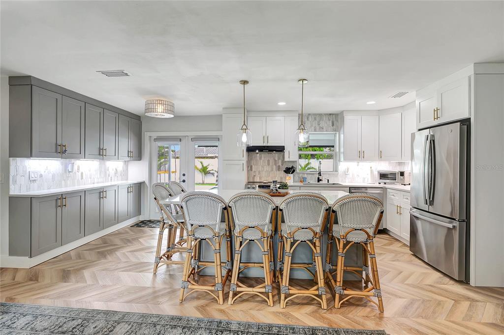 A kitchen features gray and white cabinetry, a central island with four chairs, and herringbone flooring — 510 HILLCREST DRIVE, LARGO, FL