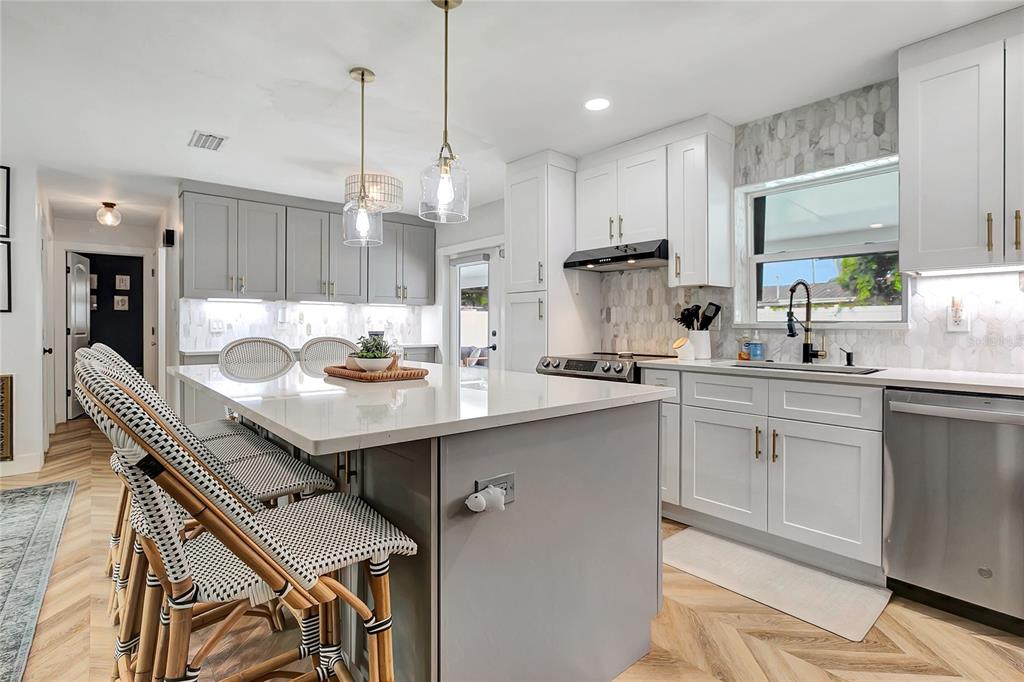 A modern kitchen features a gray island, white cabinetry, herringbone wood floors, and pendant lighting — 510 HILLCREST DRIVE, LARGO, FL