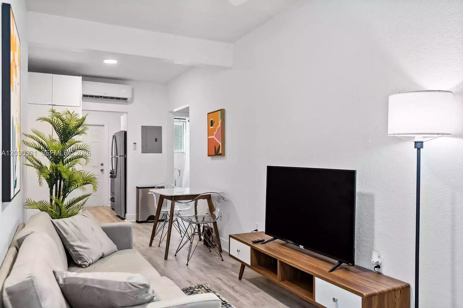 A living room features a grey sofa, a wooden media console, and a small dining area — 7325 Carlyle Ave # 2, Miami Beach FL 33141, MIAMI BEACH, FL