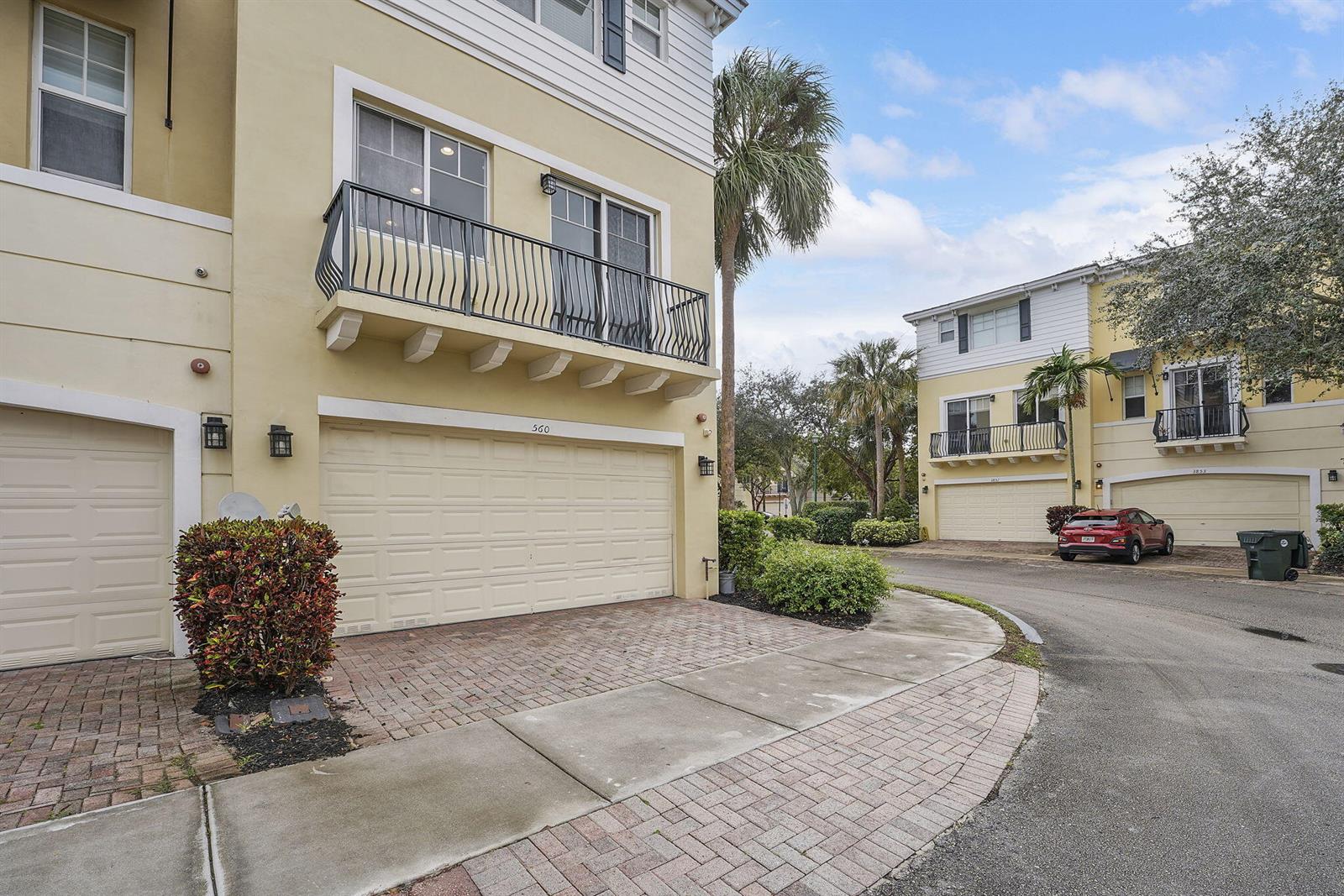 An exterior view of two multi-story townhouses with beige siding, balconies, and brick driveways — 560 NW 39th Circle # 560, Boca Raton FL 33431, BOCA RATON, FL
