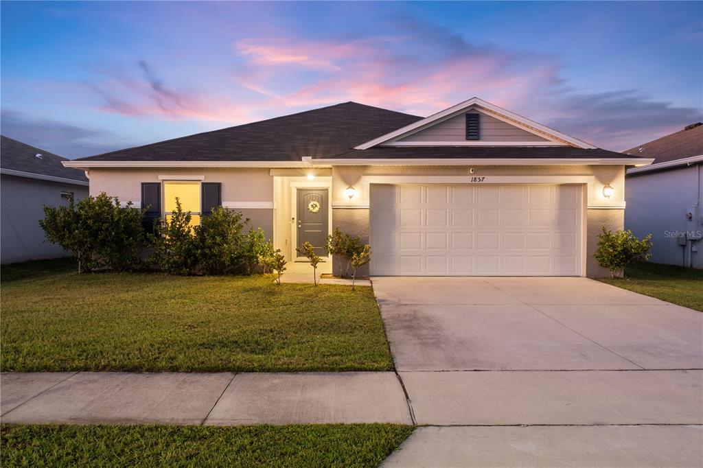 A single-story suburban house with a two-car garage and a front lawn at dusk — 1857 GOLD CREST DRIVE, ST CLOUD, FL