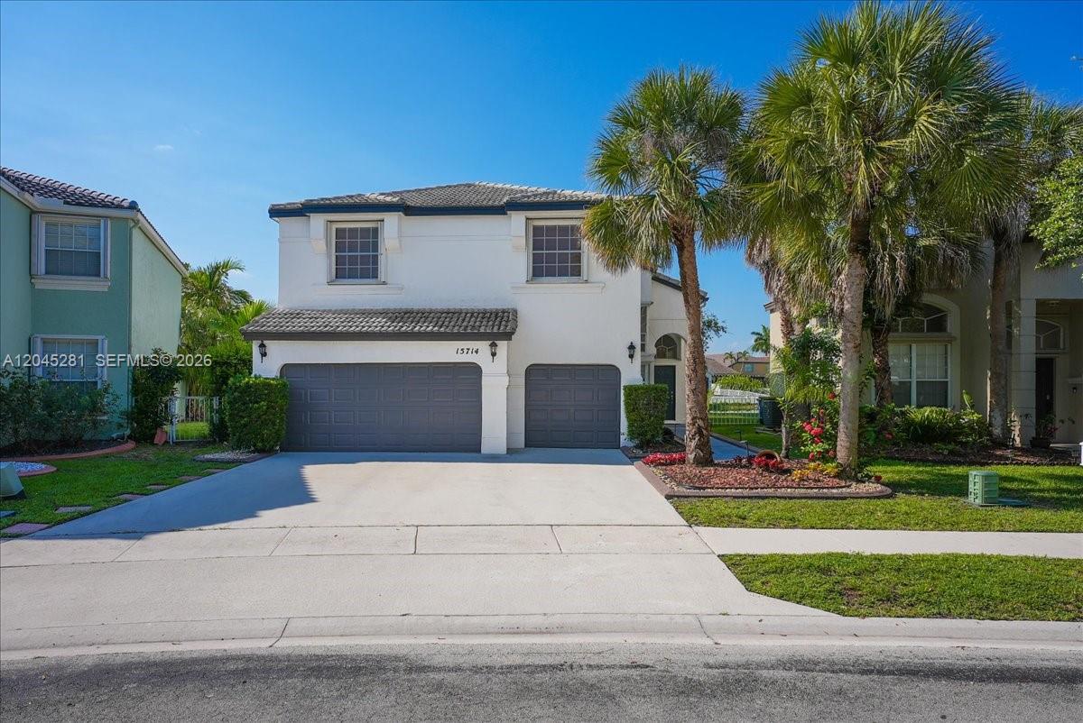 A two-story suburban house features a two-car garage, a concrete driveway, and palm trees — PEMBROKE PINES, FL