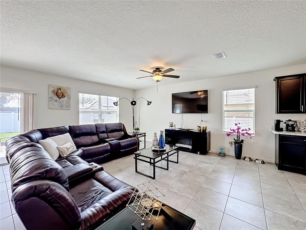 A living room features a large dark leather sectional, tiled floors, and a wall-mounted television — 1190 SW BROADVIEW STREET, PORT ST LUCIE, FL