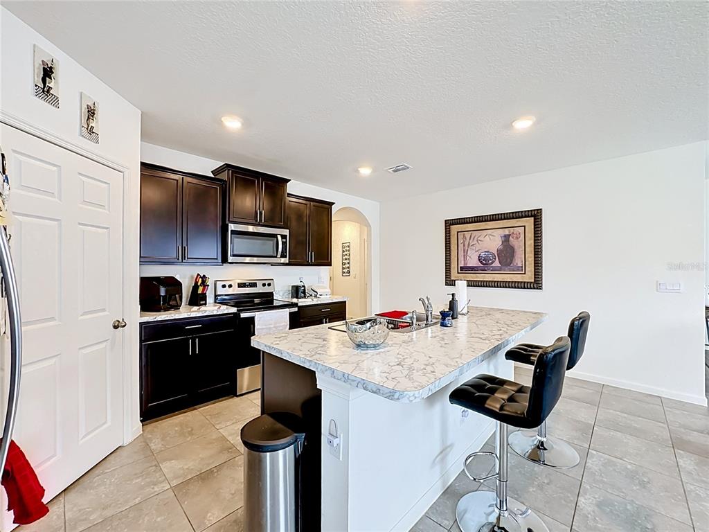 A kitchen features dark wood cabinets, a marble-patterned island, and two black bar stools — 1190 SW BROADVIEW STREET, PORT ST LUCIE, FL