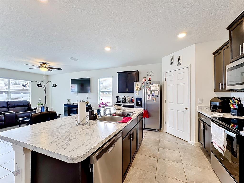A kitchen with a marble-topped island, dark wood cabinets, and stainless steel appliances — 1190 SW BROADVIEW STREET, PORT ST LUCIE, FL