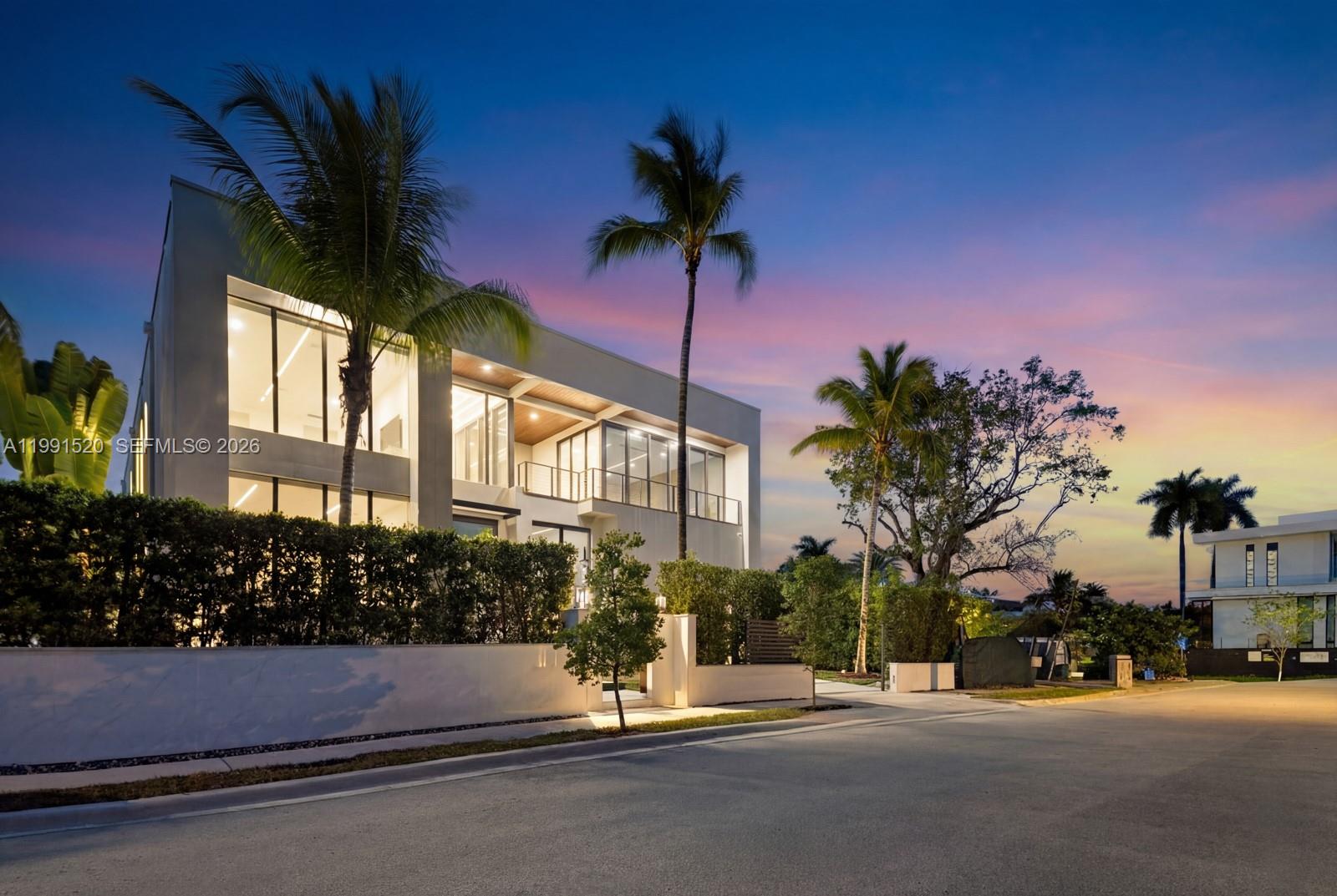 A modern multi-story home with large glass windows and palm trees at dusk — 775 NE 77th Ter, Miami FL 33138, MIAMI, FL