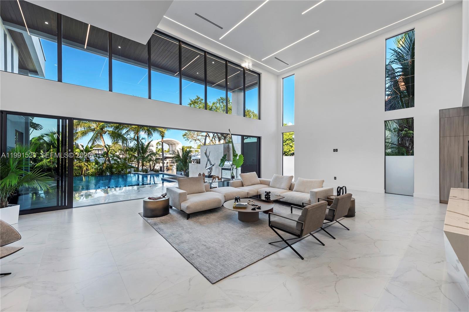 A modern living room features high ceilings, large glass walls, and a view of a pool — 775 NE 77th Ter, Miami FL 33138, MIAMI, FL