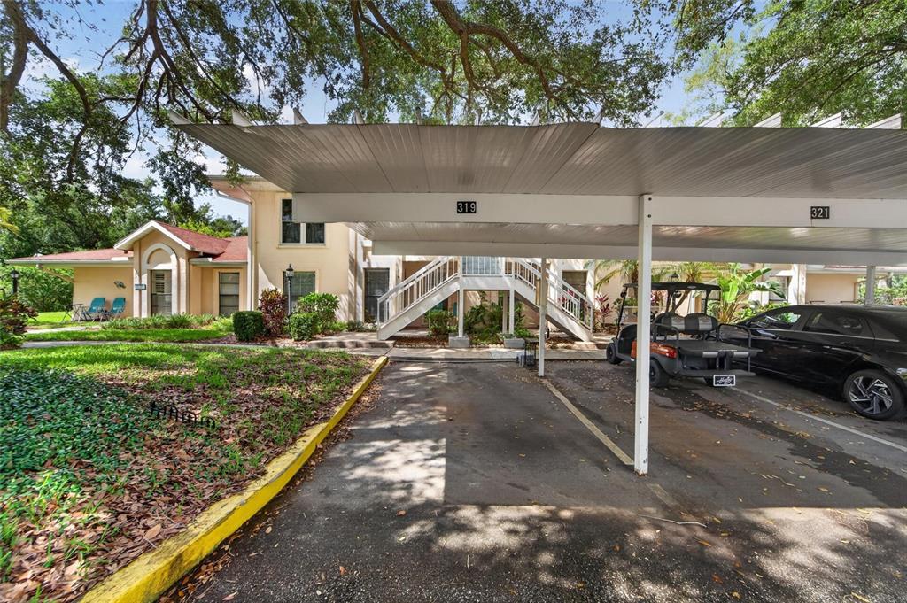 A covered carport with numbered parking spaces sits in front of a two-story apartment building — 319 KNOTTWOOD COURT UNIT 2, SUN CITY CENTER, FL