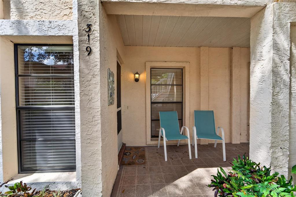 A covered patio features a tiled floor, two teal chairs, and a front door — 319 KNOTTWOOD COURT UNIT 2, SUN CITY CENTER, FL